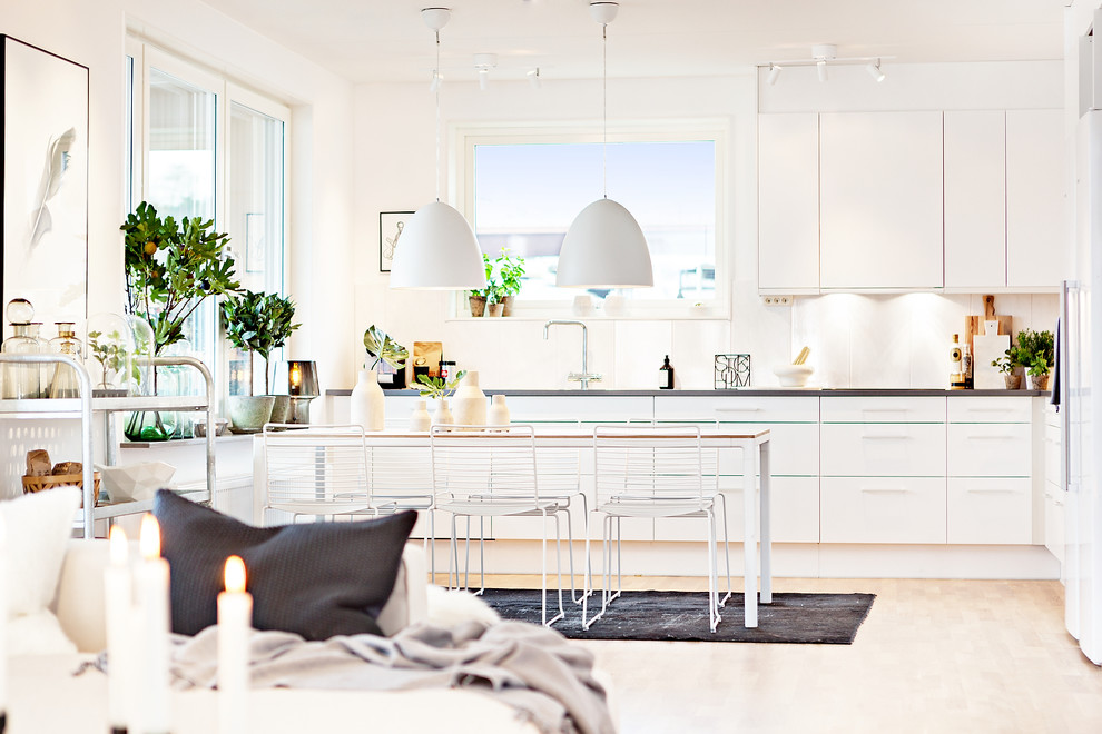 Inspiration for a large scandinavian single-wall eat-in kitchen in Gothenburg with flat-panel cabinets, white cabinets, white splashback, white appliances, light hardwood floors, no island and brown floor.