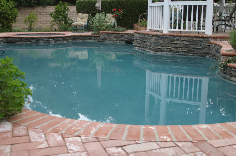 Mid-sized traditional backyard custom-shaped natural pool in Los Angeles with natural stone pavers.