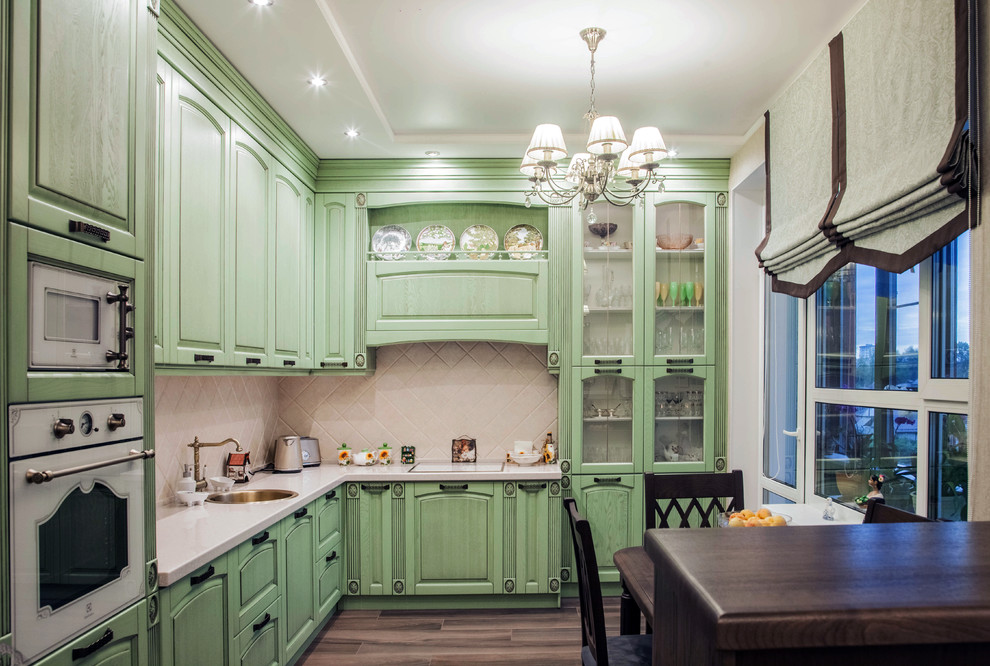 Traditional l-shaped eat-in kitchen in Other with a drop-in sink, raised-panel cabinets, green cabinets, beige splashback, medium hardwood floors, brown floor and white benchtop.