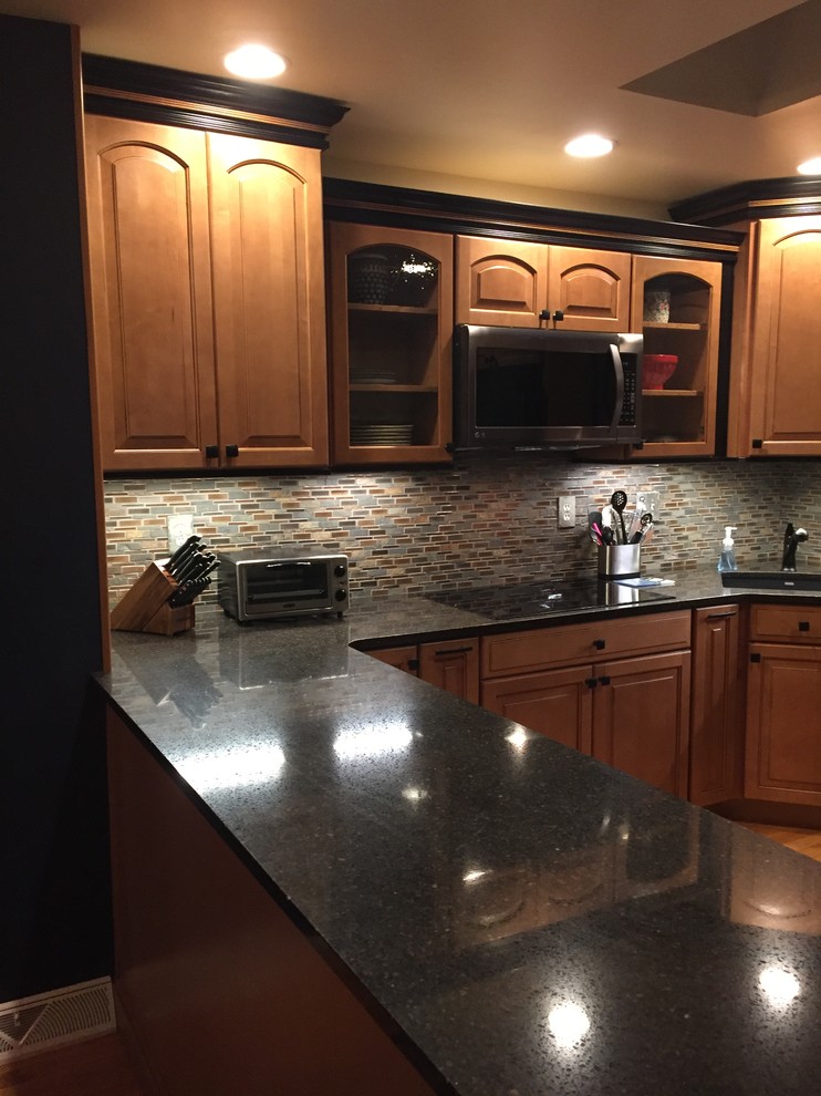 Example of a small mountain style u-shaped light wood floor kitchen design with a single-bowl sink, raised-panel cabinets, brown cabinets, quartz countertops and mosaic tile backsplash