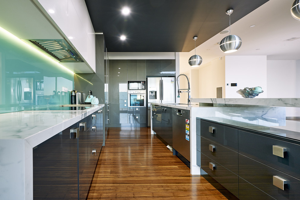 Inspiration for a large contemporary l-shaped eat-in kitchen in Melbourne with a double-bowl sink, flat-panel cabinets, marble benchtops, green splashback, glass sheet splashback, stainless steel appliances, medium hardwood floors and with island.