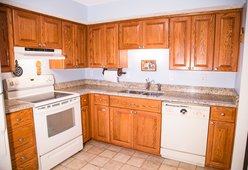 Kitchen - small rustic l-shaped kitchen idea in Baltimore with a double-bowl sink, raised-panel cabinets, medium tone wood cabinets, blue backsplash, white appliances and no island