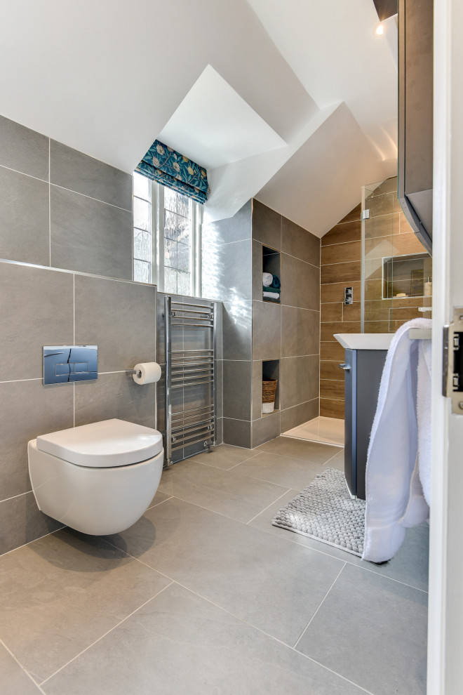 Photo of a large modern master bathroom in Sussex with flat-panel cabinets, grey cabinets, a freestanding tub, an open shower, a one-piece toilet, gray tile, ceramic tile, grey walls, ceramic floors, a drop-in sink, glass benchtops, grey floor, an open shower, white benchtops, a single vanity and a floating vanity.