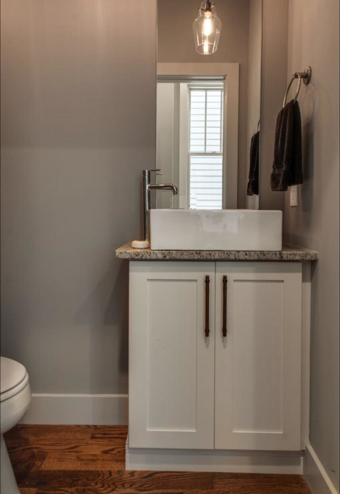 Inspiration for a small traditional powder room in Nashville with shaker cabinets, white cabinets, a two-piece toilet, grey walls, light hardwood floors, a vessel sink, granite benchtops, brown floor and grey benchtops.