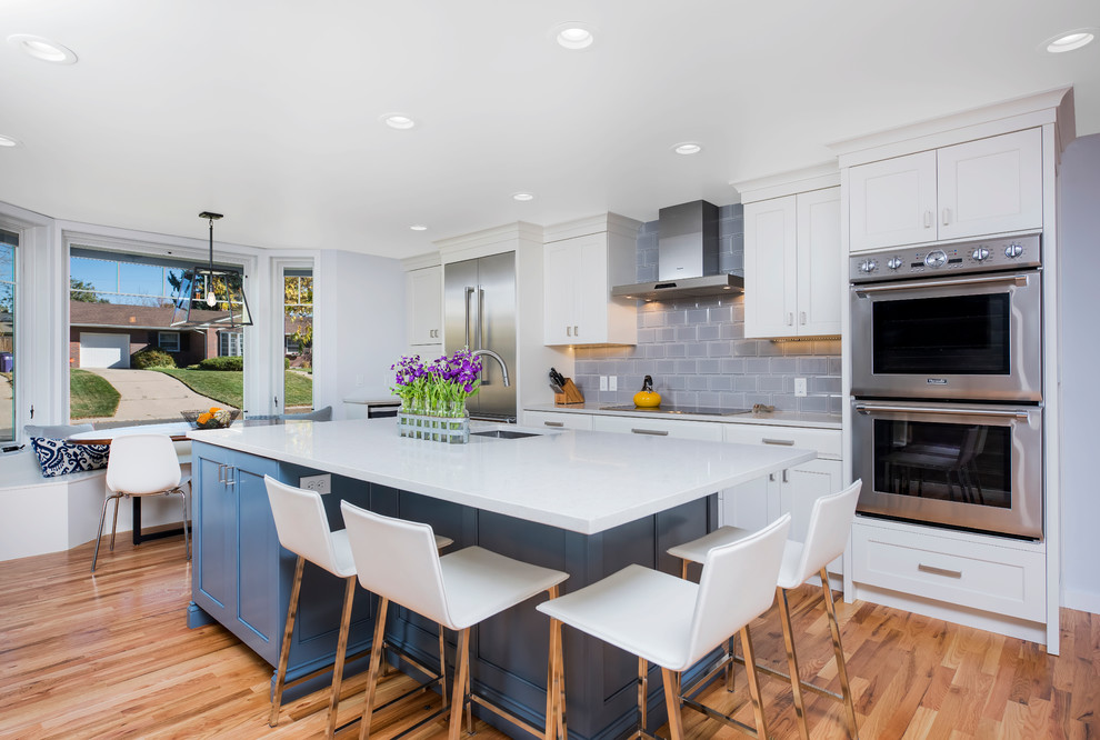 Enclosed kitchen - large transitional u-shaped light wood floor enclosed kitchen idea in Denver with a farmhouse sink, shaker cabinets, white cabinets, quartz countertops, gray backsplash, ceramic backsplash, stainless steel appliances and an island