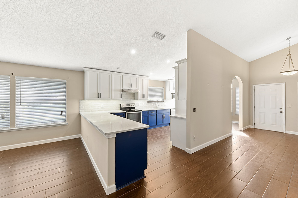 Open concept kitchen - large transitional l-shaped vinyl floor and brown floor open concept kitchen idea in Jacksonville with an undermount sink, shaker cabinets, blue cabinets, quartzite countertops, white backsplash, ceramic backsplash, stainless steel appliances and a peninsula