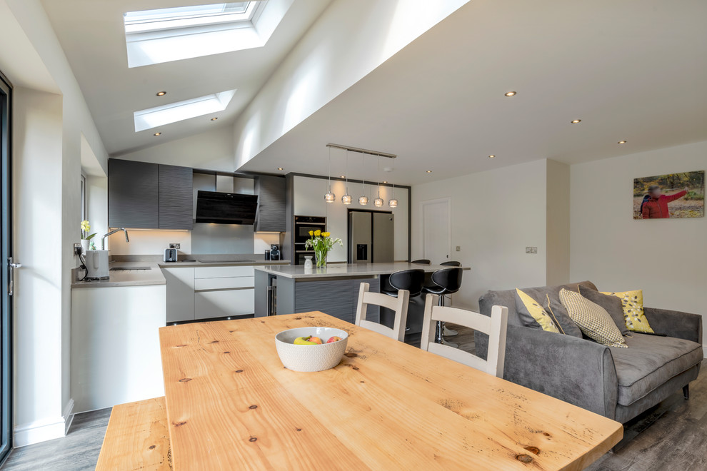Photo of a mid-sized modern open plan kitchen in Cheshire with flat-panel cabinets, quartzite benchtops, glass sheet splashback, black appliances, laminate floors, with island, grey floor and beige benchtop.