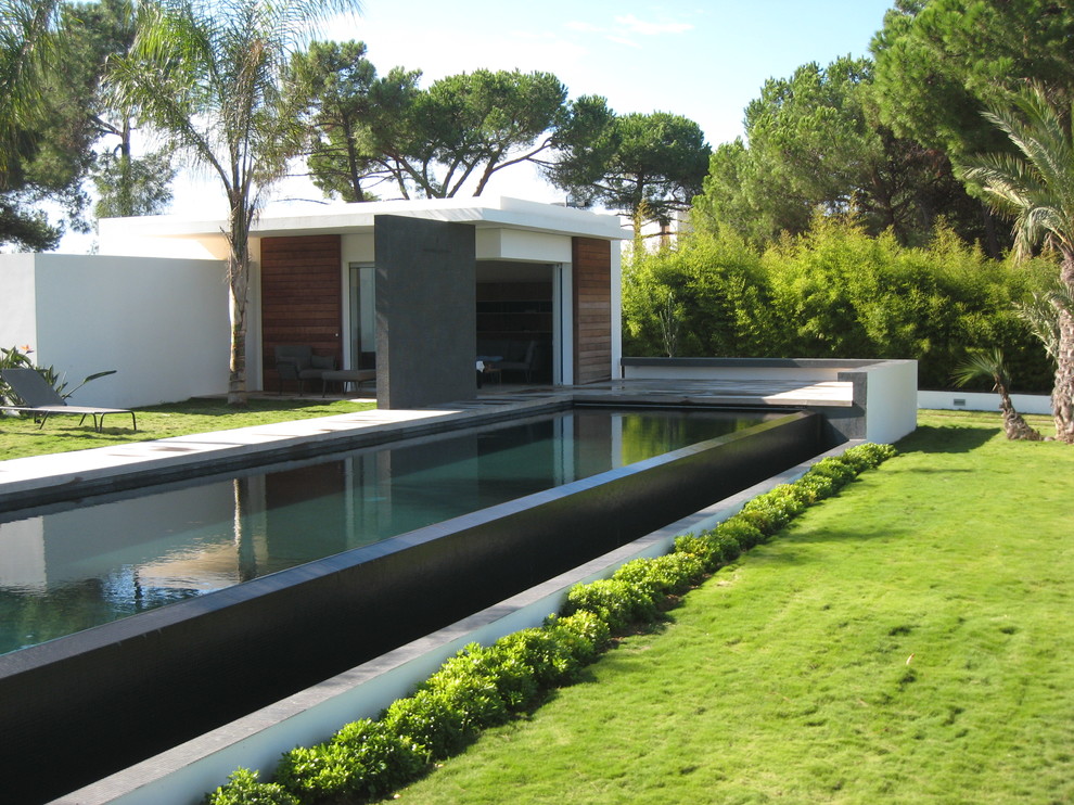 This is an example of a large contemporary backyard rectangular lap pool in Corsica with concrete slab and a pool house.