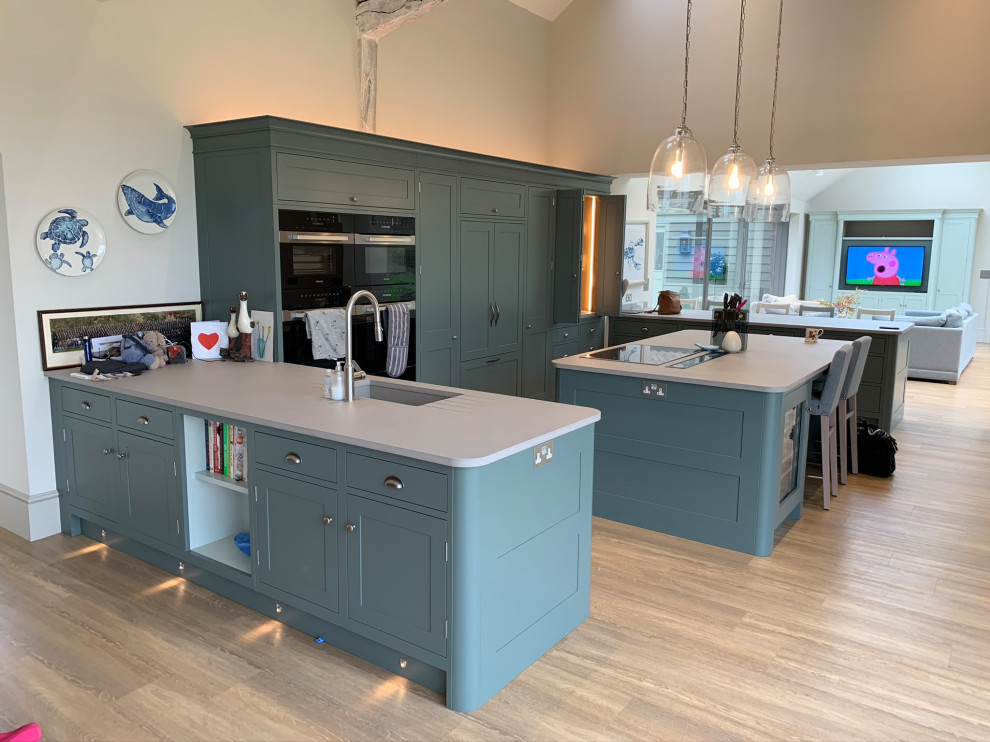 Photo of a large transitional u-shaped open plan kitchen in Cambridgeshire with an integrated sink, shaker cabinets, green cabinets, quartzite benchtops, black appliances, light hardwood floors, with island and grey benchtop.
