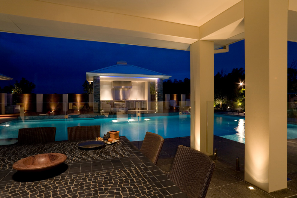 This is an example of an expansive modern backyard l-shaped pool in Sydney with natural stone pavers.