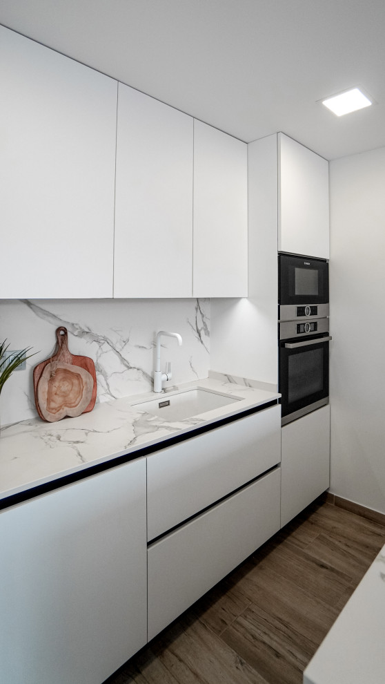 Inspiration for a mid-sized contemporary single-wall eat-in kitchen in Barcelona with an undermount sink, flat-panel cabinets, white cabinets, quartz benchtops, white splashback, engineered quartz splashback, stainless steel appliances, porcelain floors, with island, brown floor and white benchtop.