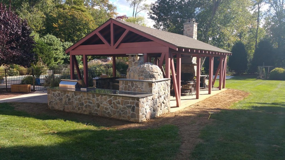 Large country backyard patio in New York with an outdoor kitchen, natural stone pavers and a pergola.