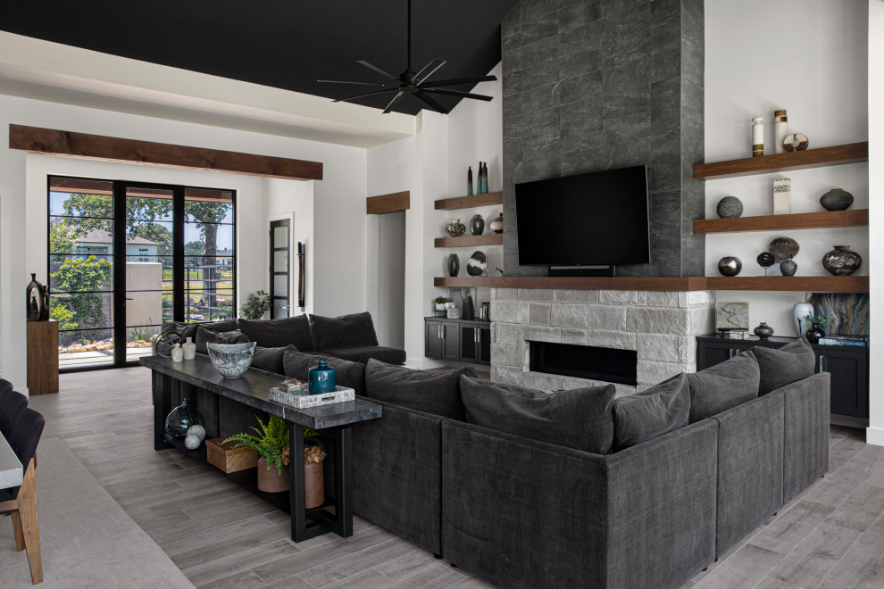 На фото: открытая гостиная комната в стиле модернизм с белыми стенами, стандартным камином, фасадом камина из камня, телевизором на стене и сводчатым потолком