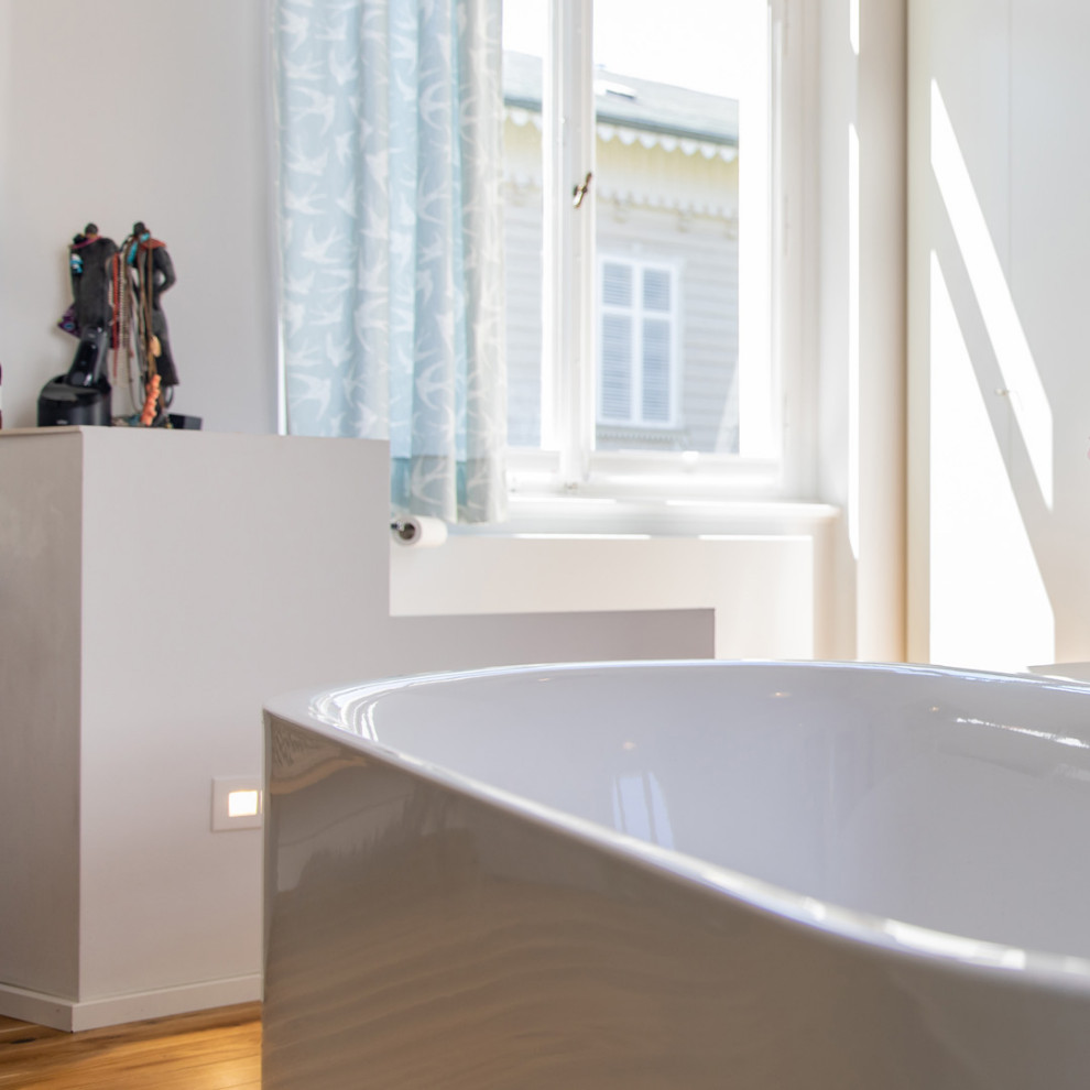Modernes Badezimmer mit weißen Schränken, freistehender Badewanne, bodengleicher Dusche, Wandtoilette, hellem Holzboden, Aufsatzwaschbecken, offener Dusche und eingebautem Waschtisch in Düsseldorf