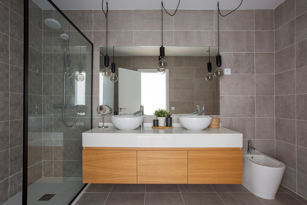 This is an example of a contemporary bathroom in Madrid with flat-panel cabinets, medium wood cabinets, a built-in shower, grey tiles, grey walls, a vessel sink, grey floors, an open shower, white worktops, double sinks and a floating vanity unit.