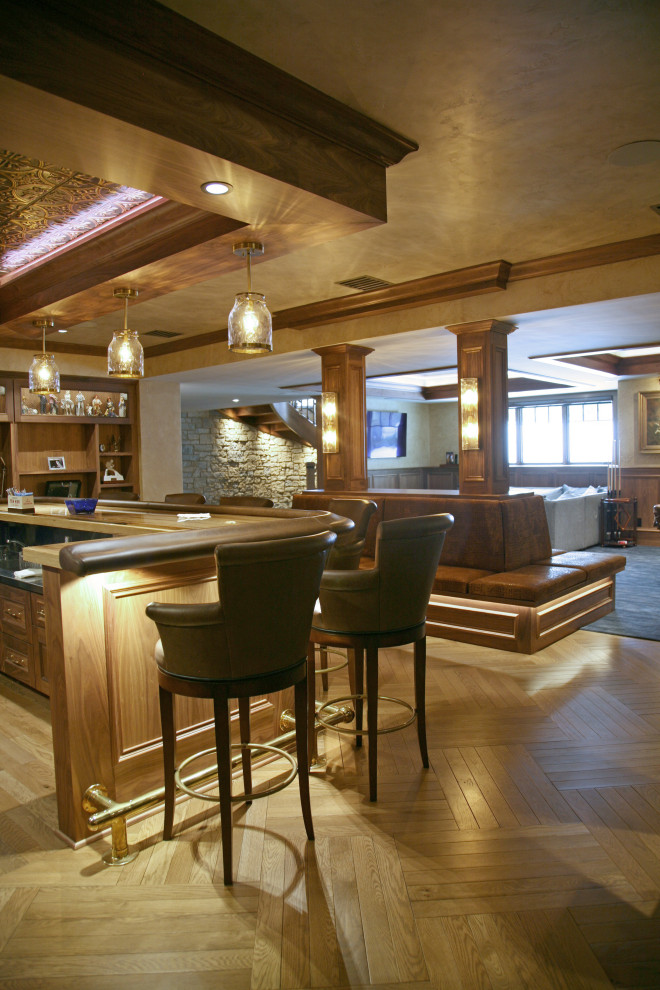 Inspiration for an expansive traditional u-shaped home bar in Milwaukee with an integrated sink, raised-panel cabinets, medium wood cabinets, granite benchtops, brown splashback, timber splashback, light hardwood floors, brown floor and black benchtop.
