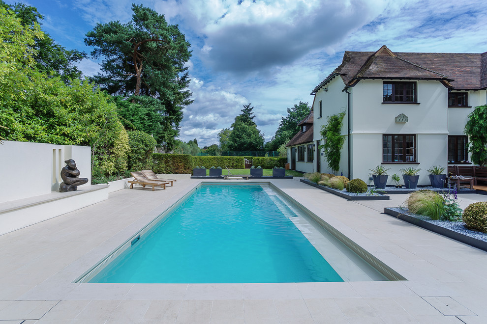 This is an example of a traditional backyard rectangular lap pool in Hampshire with a pool house and tile.