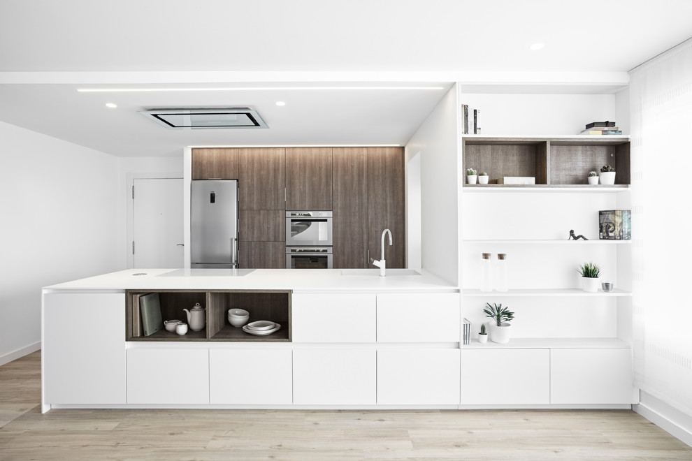 Photo of a modern galley kitchen in Other with an undermount sink, flat-panel cabinets, white cabinets, stainless steel appliances, light hardwood floors, a peninsula and beige floor.