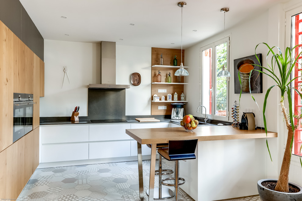 Photo of a mid-sized contemporary l-shaped eat-in kitchen in Paris with an undermount sink, flat-panel cabinets, light wood cabinets, white splashback, white appliances, ceramic floors and with island.