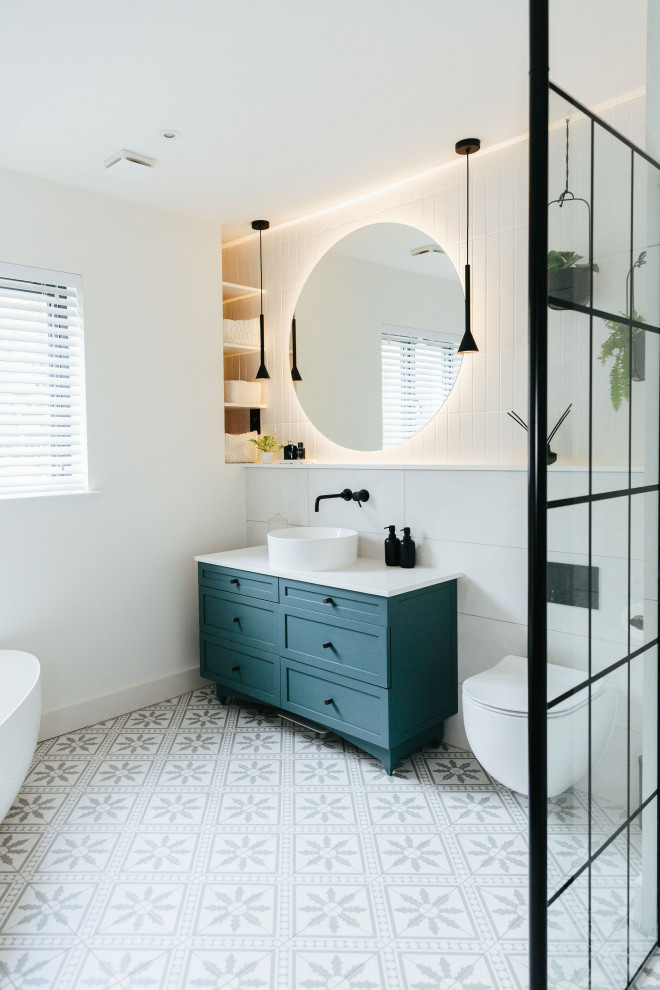 Photo of a large transitional kids bathroom in London with shaker cabinets, blue cabinets, a freestanding tub, an open shower, a wall-mount toilet, white tile, marble, white walls, mosaic tile floors, a drop-in sink, marble benchtops, multi-coloured floor, an open shower, white benchtops, a single vanity, a built-in vanity and brick walls.