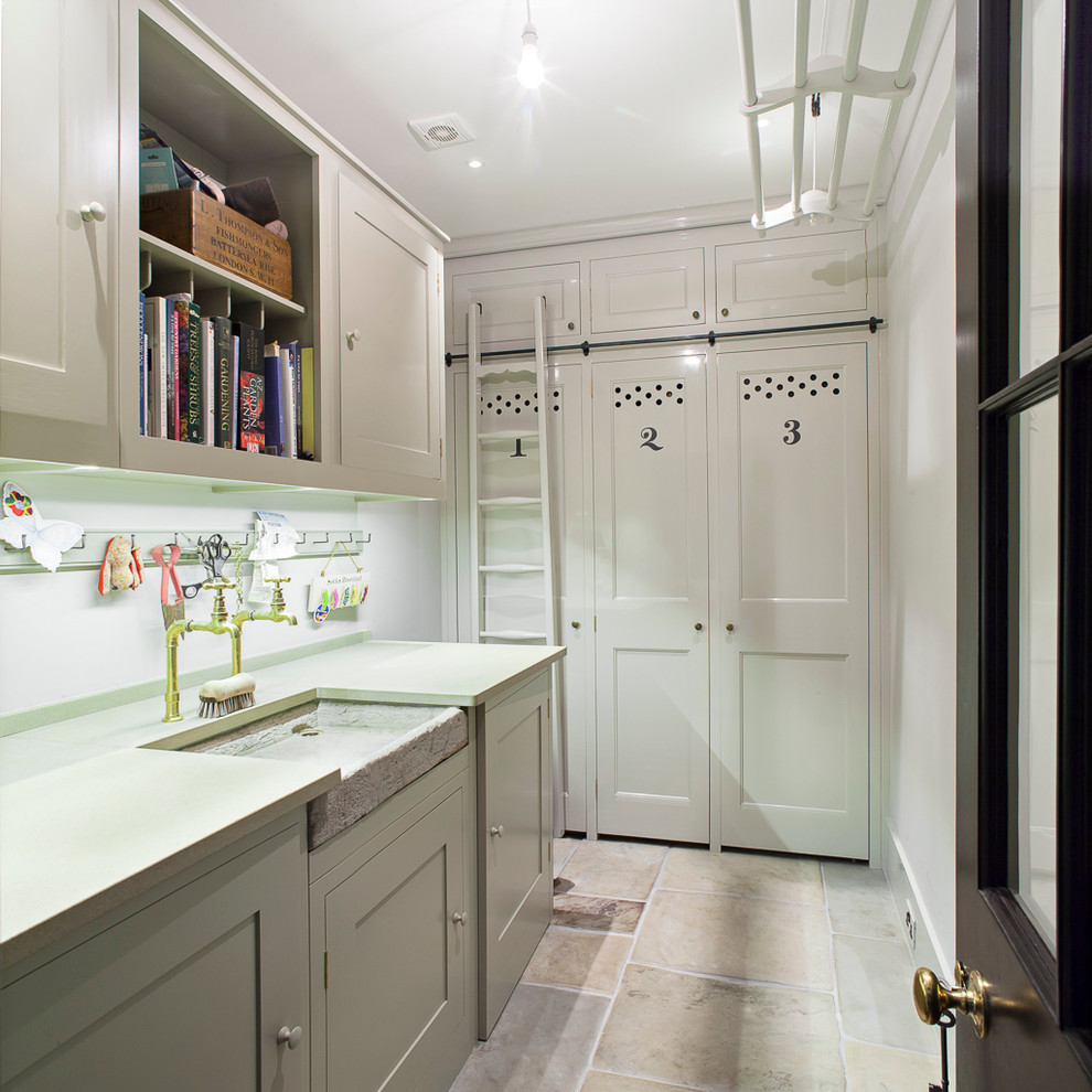 Inspiration for a large traditional dedicated laundry room in London with a farmhouse sink, shaker cabinets, white cabinets, white walls and a concealed washer and dryer.