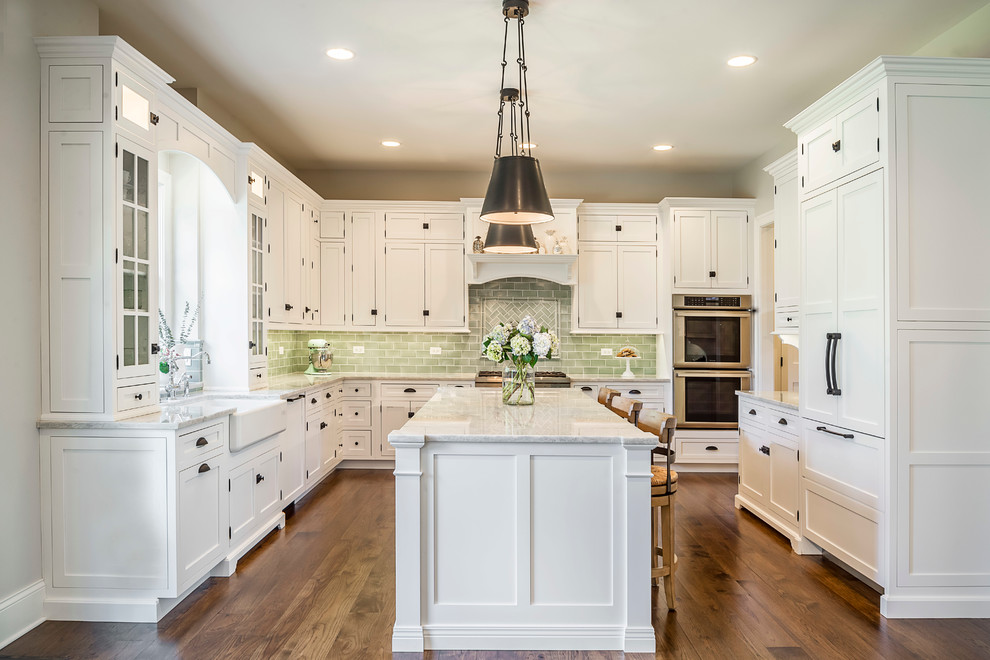 Design ideas for a traditional l-shaped eat-in kitchen in Chicago with a farmhouse sink, shaker cabinets, white cabinets, quartzite benchtops, green splashback, ceramic splashback, panelled appliances, medium hardwood floors and with island.