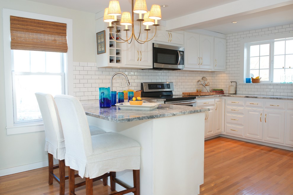 Design ideas for a mid-sized traditional u-shaped eat-in kitchen in Boston with an undermount sink, raised-panel cabinets, white cabinets, quartzite benchtops, white splashback, ceramic splashback, stainless steel appliances, medium hardwood floors, a peninsula and brown floor.