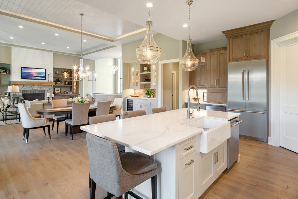 Mid-sized transitional l-shaped medium tone wood floor and gray floor eat-in kitchen photo in Cincinnati with a farmhouse sink, recessed-panel cabinets, medium tone wood cabinets, quartz countertops, white backsplash, ceramic backsplash, stainless steel appliances, an island and white countertops