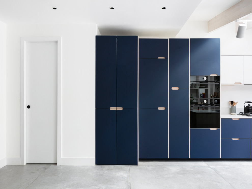 Photo of a mid-sized scandinavian galley open plan kitchen in London with a drop-in sink, flat-panel cabinets, blue cabinets, solid surface benchtops, white splashback, granite splashback, black appliances, porcelain floors, no island, grey floor, white benchtop and exposed beam.