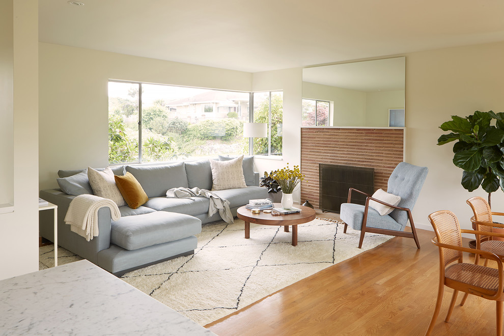 Photo of a small midcentury open concept living room in Seattle with white walls, medium hardwood floors, a standard fireplace, a brick fireplace surround, no tv and brown floor.