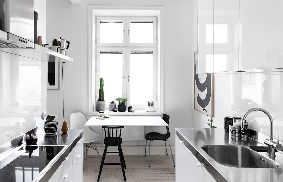 Small transitional u-shaped eat-in kitchen in Madrid with a single-bowl sink, flat-panel cabinets, white cabinets, white splashback, medium hardwood floors, no island and stainless steel benchtops.