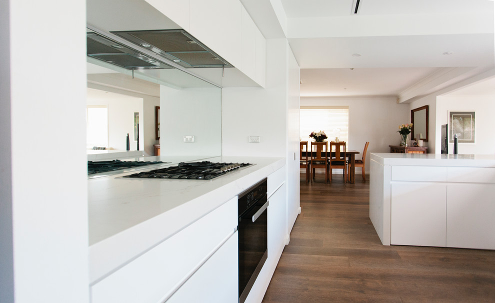 Photo of a large u-shaped open plan kitchen in Sydney with an undermount sink, louvered cabinets, white cabinets, granite benchtops, glass sheet splashback, stainless steel appliances and light hardwood floors.
