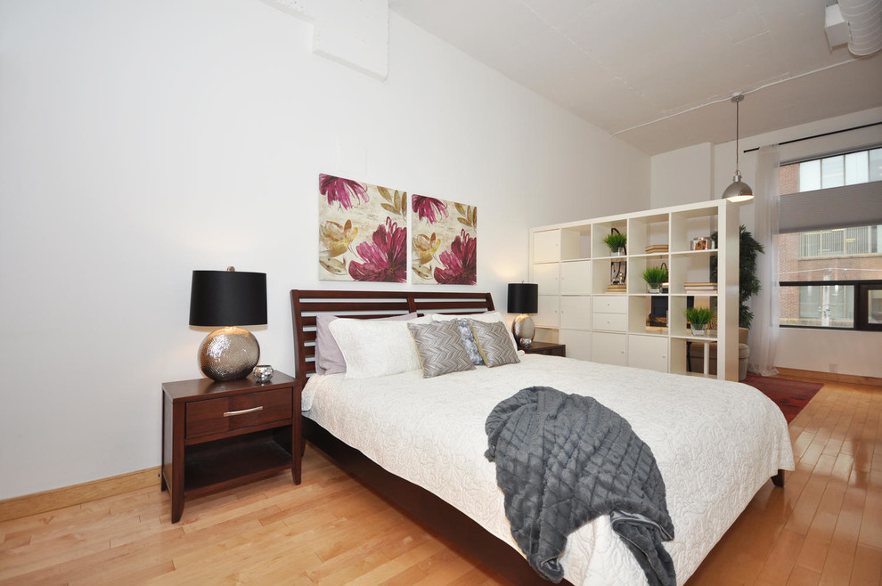 Mid-sized industrial loft-style bedroom in Toronto with white walls and light hardwood floors.
