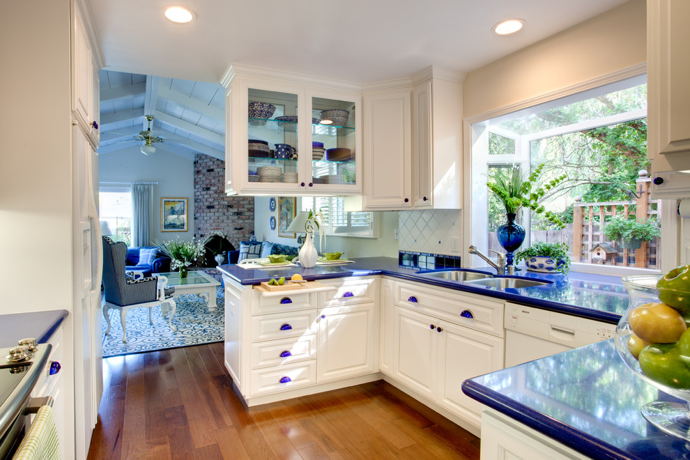 Photo of a small transitional galley open plan kitchen in San Francisco with an undermount sink, raised-panel cabinets, white cabinets, quartz benchtops, ceramic splashback, white splashback, stainless steel appliances, medium hardwood floors and blue benchtop.