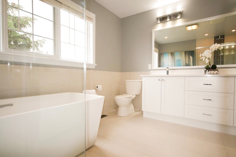 Photo of a large modern master bathroom in Ottawa with flat-panel cabinets, white cabinets, a freestanding tub, a corner shower, a two-piece toilet, beige tile, porcelain tile, grey walls, porcelain floors, an undermount sink, engineered quartz benchtops, beige floor and a sliding shower screen.