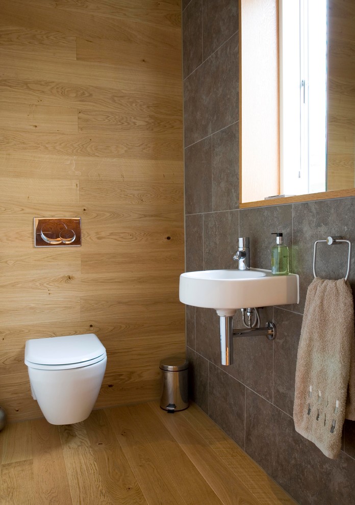 Photo of a small contemporary powder room in Edinburgh with a wall-mount sink, a wall-mount toilet, porcelain tile, light hardwood floors and gray tile.
