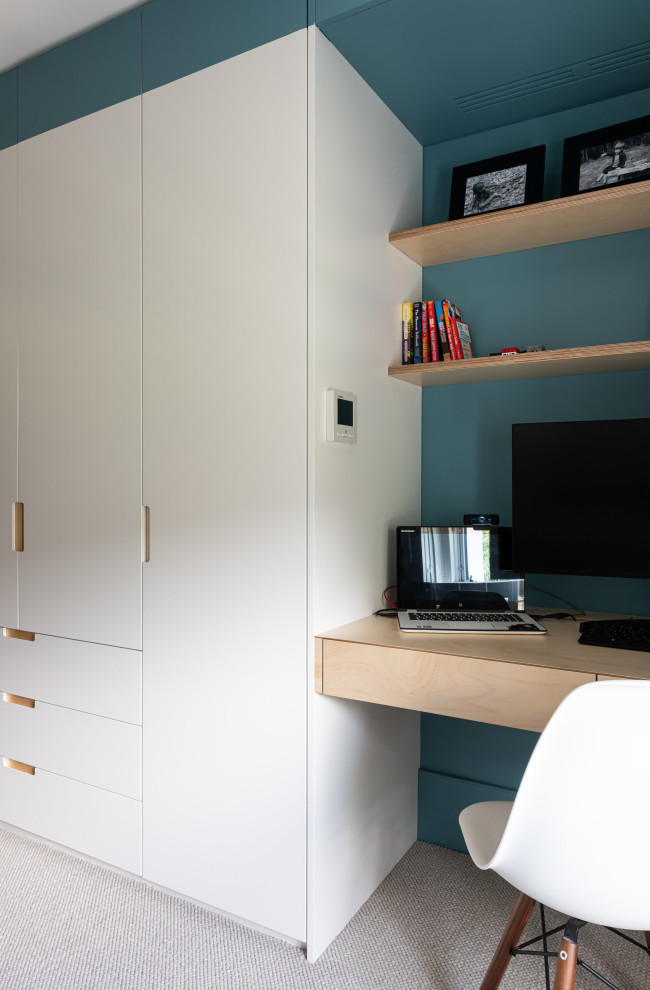Modelo de despacho actual de tamaño medio con paredes azules, moqueta, escritorio empotrado y suelo beige