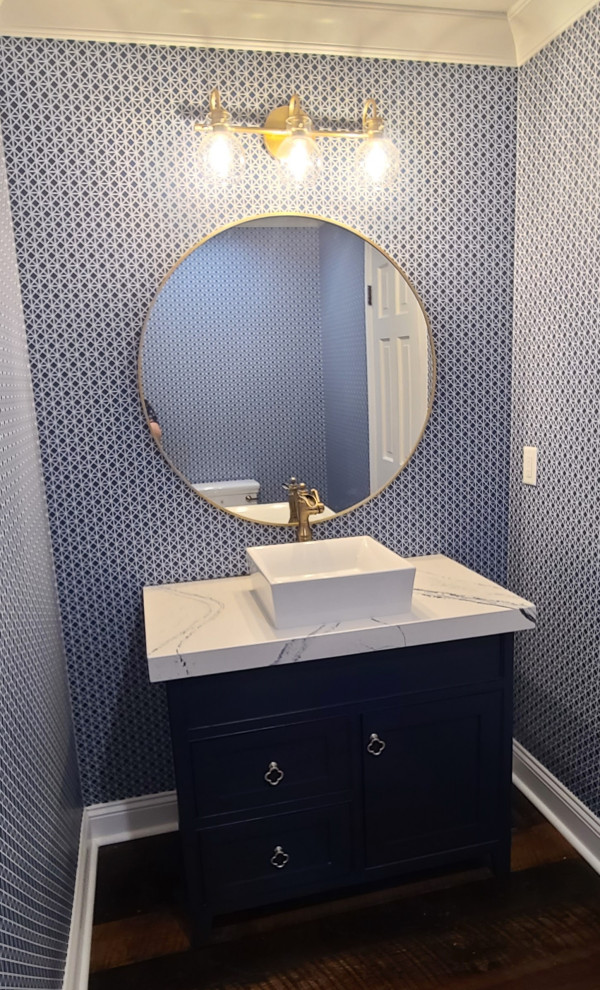 Aménagement d'une salle de bain avec des portes de placard bleues, un mur bleu, parquet foncé, une vasque, un plan de toilette en quartz, un plan de toilette blanc, meuble simple vasque, meuble-lavabo sur pied et du papier peint.