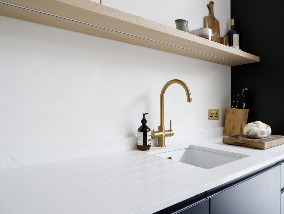 Esempio di una cucina design di medie dimensioni con lavello da incasso, ante lisce, ante nere, top in quarzite, paraspruzzi bianco, elettrodomestici neri, pavimento in cemento, pavimento grigio e top bianco
