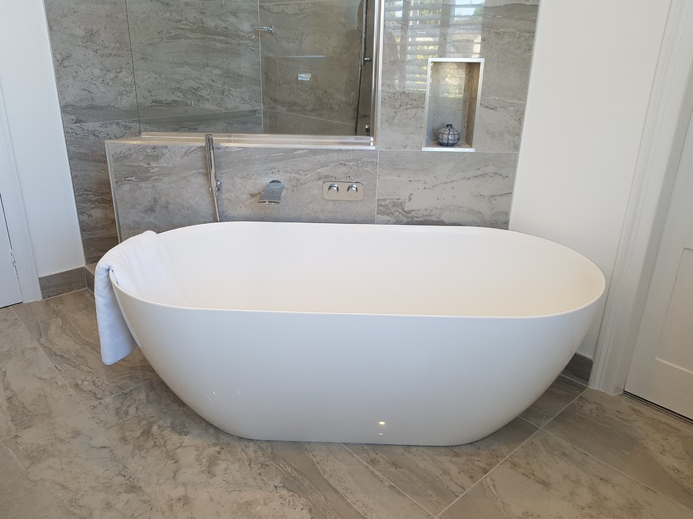 This is an example of a large contemporary bathroom in Other with flat-panel cabinets, white cabinets, a freestanding bath, a wall mounted toilet, grey tiles, porcelain tiles, grey walls, porcelain flooring, a wall-mounted sink, marble worktops, grey floors, an open shower and white worktops.
