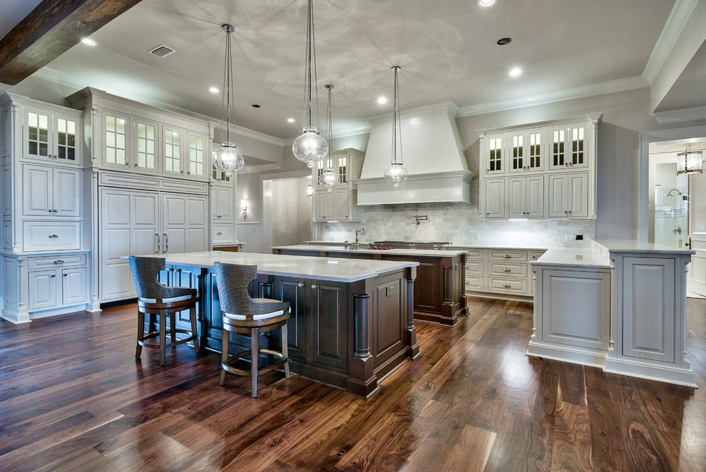 This is an example of a large traditional eat-in kitchen in Miami with a single-bowl sink, white cabinets, marble benchtops, multi-coloured splashback, stainless steel appliances, medium hardwood floors and multiple islands.