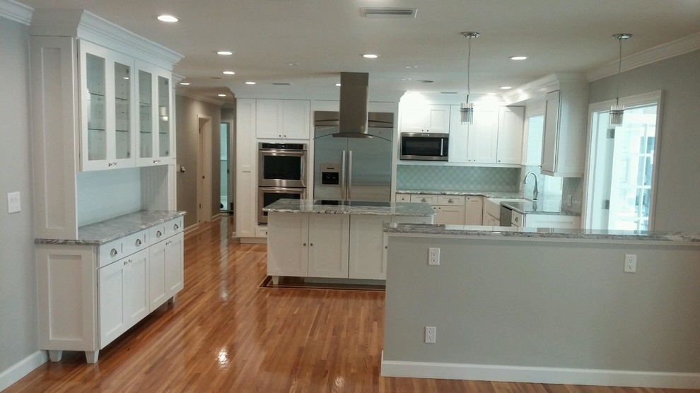 This is an example of a large beach style l-shaped kitchen in Orlando with a farmhouse sink, shaker cabinets, white cabinets, granite benchtops, blue splashback, ceramic splashback, stainless steel appliances, medium hardwood floors and with island.