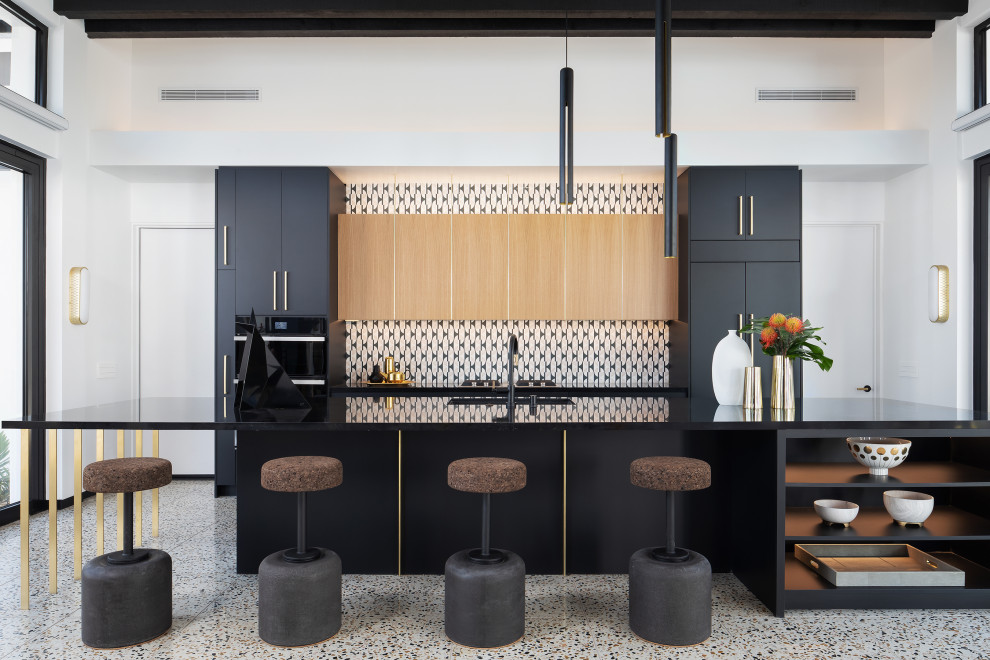 This is an example of a large midcentury single-wall eat-in kitchen in Los Angeles with flat-panel cabinets, black cabinets, multi-coloured splashback, stone tile splashback, black appliances, terrazzo floors, with island and black benchtop.