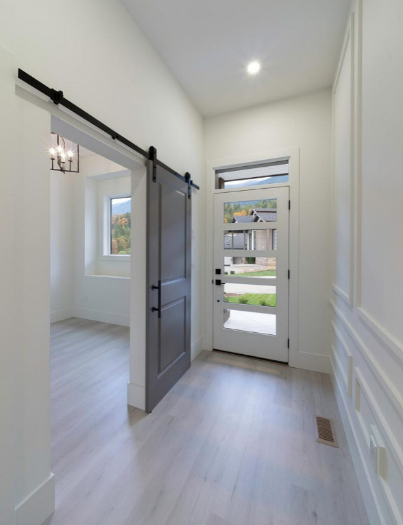 Immagine di un ingresso stile americano di medie dimensioni con pareti bianche, pavimento in laminato, una porta singola, una porta bianca, pavimento beige e pannellatura