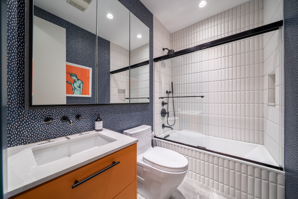 Exemple d'une salle de bain principale tendance de taille moyenne avec un placard à porte shaker, des portes de placard oranges, un carrelage blanc, un plan de toilette en quartz modifié, un plan de toilette blanc, meuble simple vasque, meuble-lavabo encastré, une baignoire en alcôve, un combiné douche/baignoire, WC à poser, un mur bleu, un sol en carrelage de porcelaine, un lavabo encastré, un sol blanc, une cabine de douche à porte coulissante et du papier peint.
