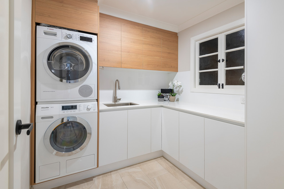 Mid-sized contemporary l-shaped dedicated laundry room in Brisbane with an undermount sink, light wood cabinets, quartz benchtops, light hardwood floors, a stacked washer and dryer and white benchtop.