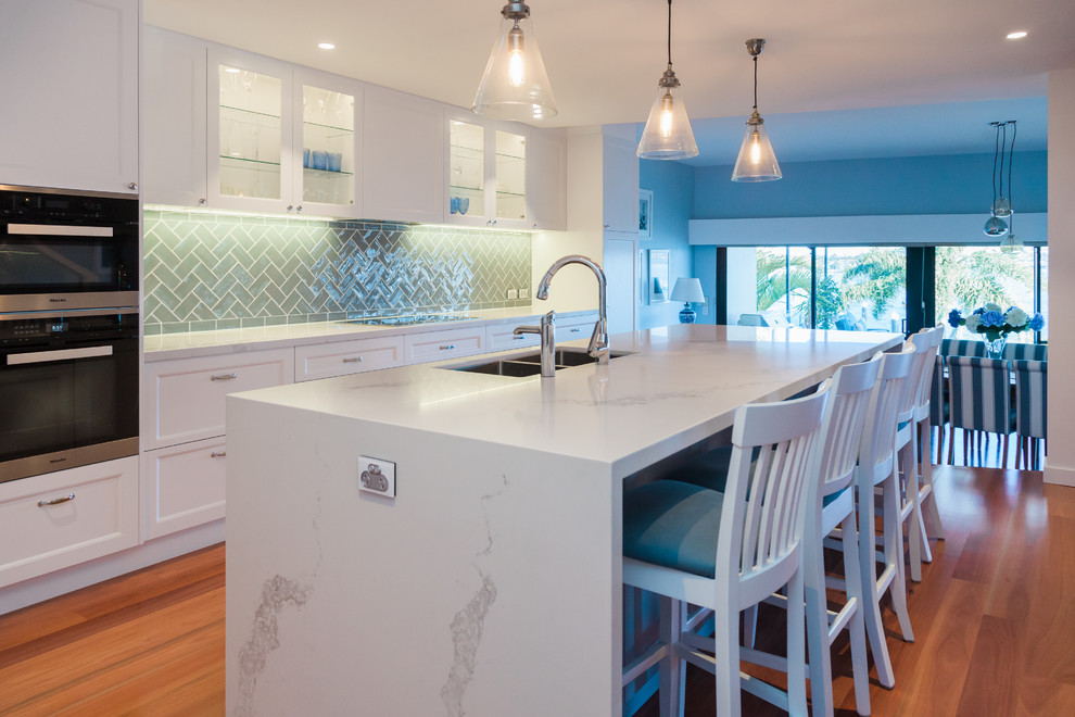 Inspiration for a large beach style galley kitchen pantry in Sydney with an undermount sink, shaker cabinets, white cabinets, quartz benchtops, green splashback, ceramic splashback, stainless steel appliances, medium hardwood floors and with island.
