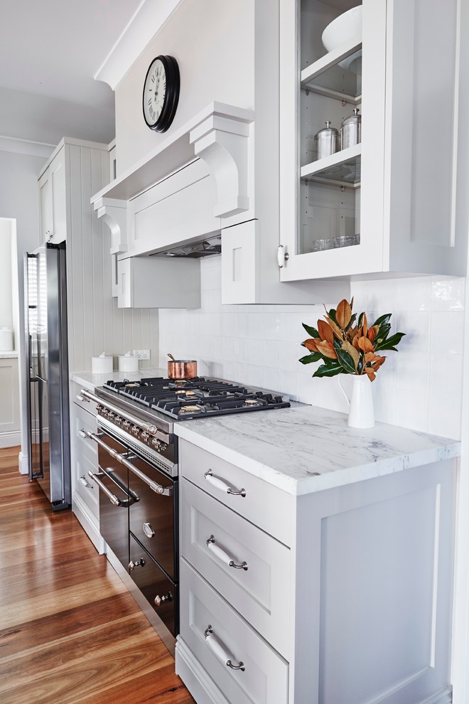 Photo of a mid-sized traditional l-shaped eat-in kitchen in Sydney with a farmhouse sink, shaker cabinets, grey cabinets, white splashback, stainless steel appliances, medium hardwood floors and with island.
