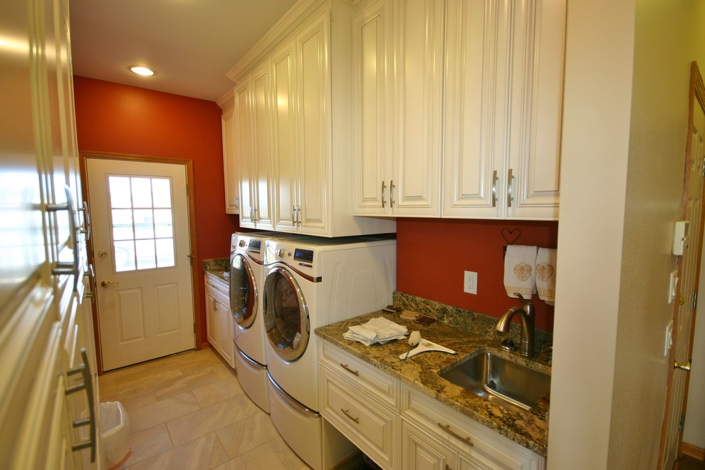 Photo of a small modern single-wall utility room in Milwaukee with an undermount sink, raised-panel cabinets, white cabinets, granite benchtops, beige splashback, stone tile splashback, porcelain floors, red walls and a side-by-side washer and dryer.
