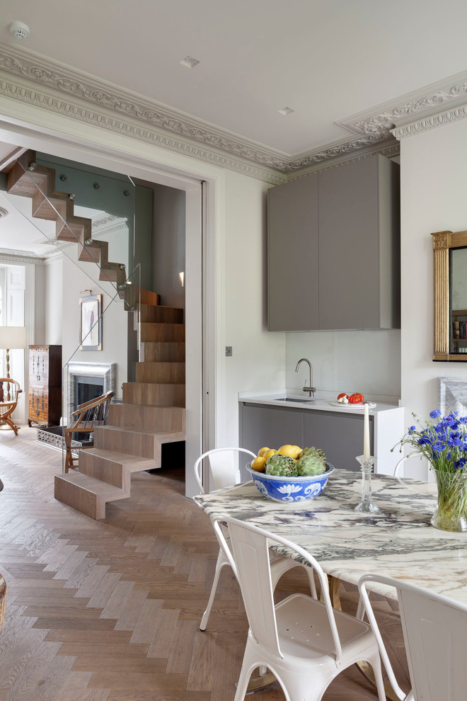 This is an example of a mid-sized eclectic kitchen/dining combo in London with grey walls, medium hardwood floors, a standard fireplace, a stone fireplace surround and brown floor.